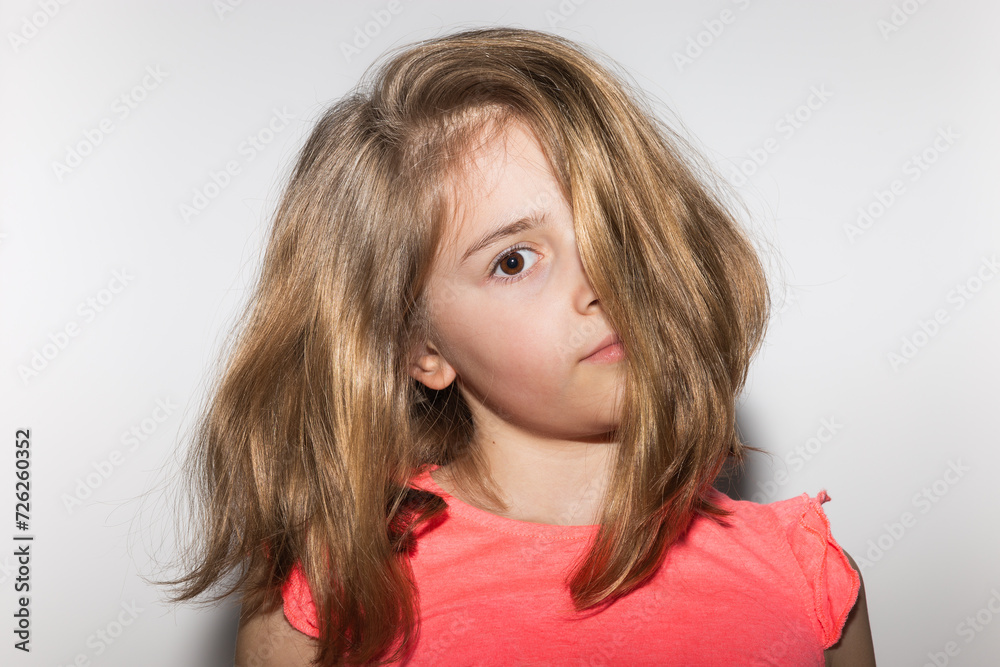 Cute little 8 years old girl with serious gesture, salmon colored t-shirt and blond hair covering half of her face on white background. Children and childhood concept Cute little 8 years old girl with serious gesture, salmon colored t-shirt and blond hair covering half of her face on white background. Children and childhood concept