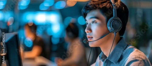 Asian male customer care service worker working late at office call center, collaborating with colleagues for success.