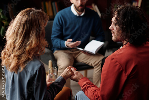 High angle selective focus shot of young man and woman holding hands at family psychotherapy session photo