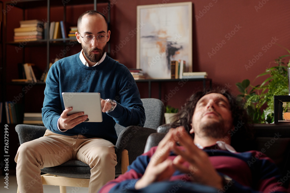 Selective focus shot of modern Middle Eastern psychologist taking notes on digital tablet while working with patient Selective focus shot of modern Middle Eastern psychologist taking notes on digital tablet while working with patient