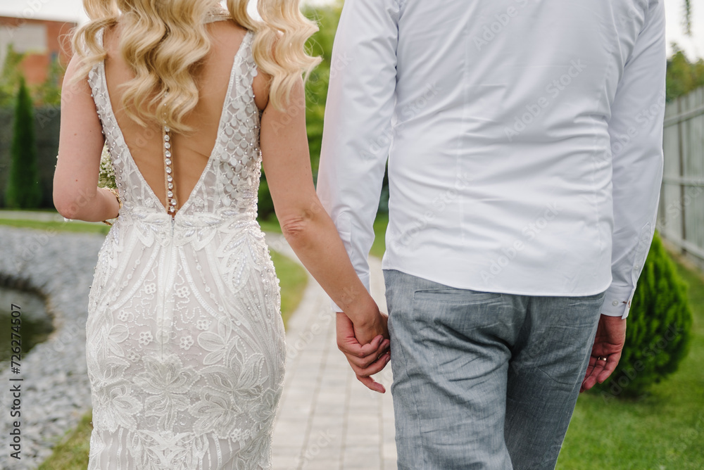 Bride and groom hold hands and walking on the street. Closeup. Details of wedding moments. Newlyweds together. Bride and groom walk outdoors. Back down view. Couple hands. Bride and groom hold hands and walking on the street. Closeup. Details of wedding moments. Newlyweds together. Bride and groom walk outdoors. Back down view. Couple hands.