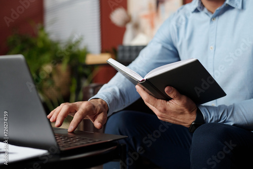 Unrecognizable man holding notebook searching information in Internet on laptop photo