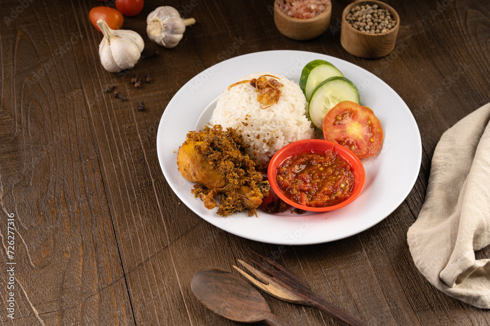 Ayam Goreng Lengkuas Kremes or Crispy Galangal Fried Chicken with steamed rice and chili paste or sambal on white plate and wood table