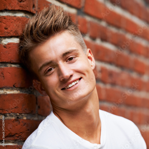 Smile, portrait and young man on a brick wall in the city to relax and explore in Australia with pride. Happy, face and male person or student on an urban background with confidence while relaxing