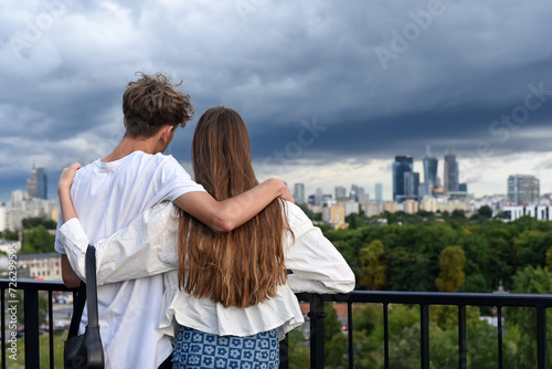 a guy and a girl, hugging each other, stand on the roof of a building, admiring the beautiful view of the city landscape