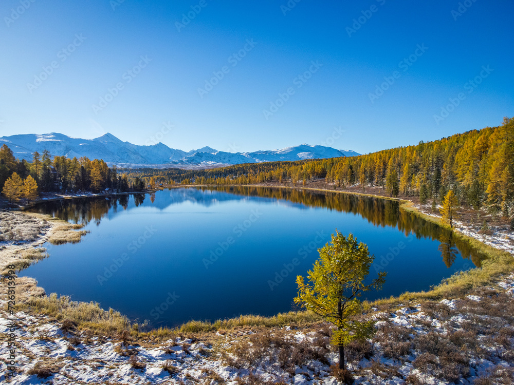 Breathtaking aerial shot capturing a tranquil mountain lake surrounded by autumn colors and snow dust in Altai.