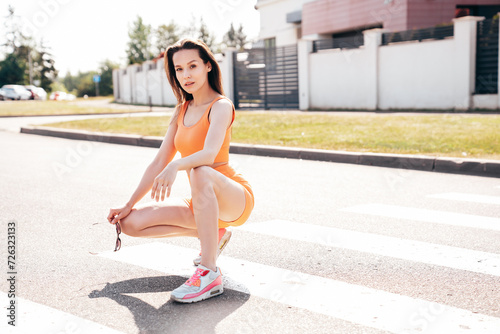 Young beautiful confident female in trendy summer cycling shorts and tank top clothes. Carefree woman posing in street. Positive model having fun. Cheerful and happy. Sits on asphalt