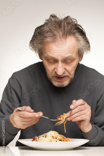 Older man eating spaghetti with minced meat, tomatoes and cheese
