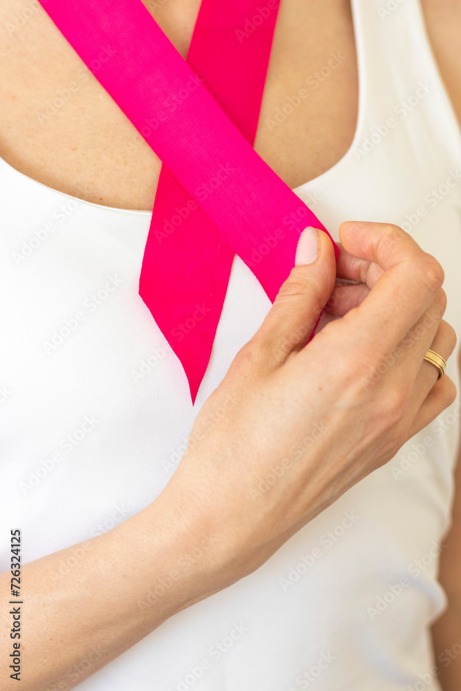 Shot of the woman in the white top against the white wall, with pink ribbon on her neck as a symbol of breast cancer awareness. Concept Shot of the woman in the white top against the white wall, with pink ribbon on her neck as a symbol of breast cancer awareness. Concept