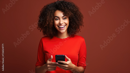 African American woman, red shirt, using phone with happiness, red background