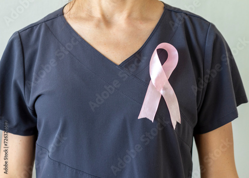 Shot of the female doctor against the white wall with pink ribbon, as a symbol of a breast cancer awareness. Concept