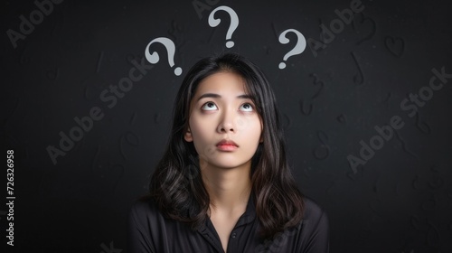 Young woman contemplating with question marks above her head, representing curiosity or confusion in decision making photo