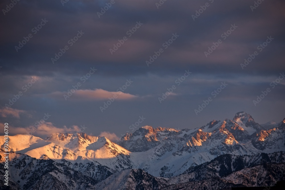 Beautiful view to the snowy winter mountain tops cloudy sky and golden hour sunlight