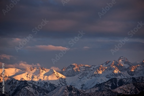 Beautiful view to the snowy winter mountain tops cloudy sky and golden hour sunlight © Marina Seagull