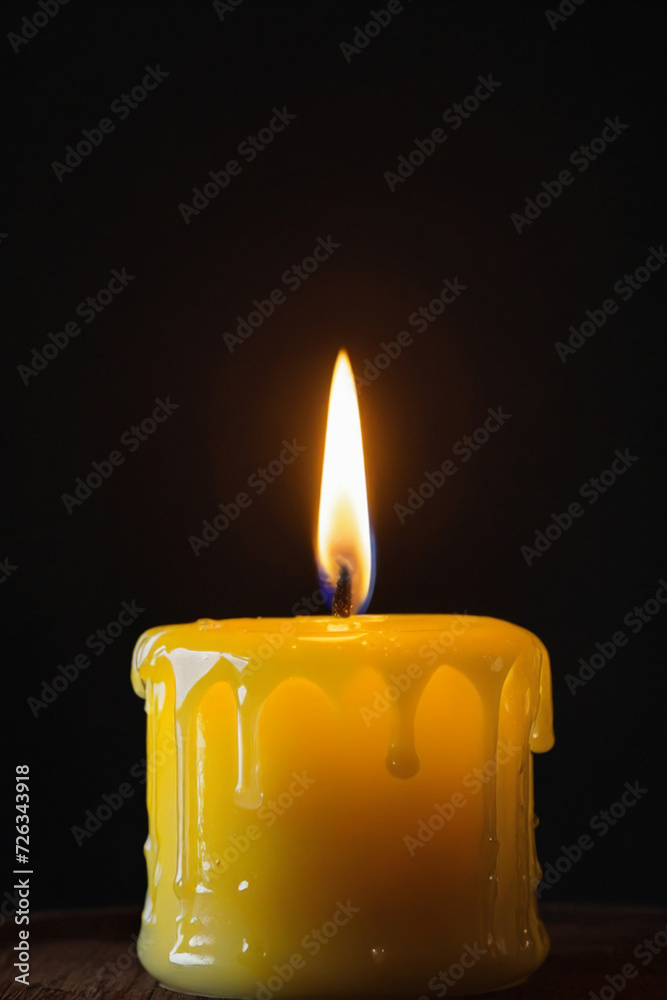 Yellow candle burning with streaks of paraffin on dark background Yellow candle burning with streaks of paraffin on dark background