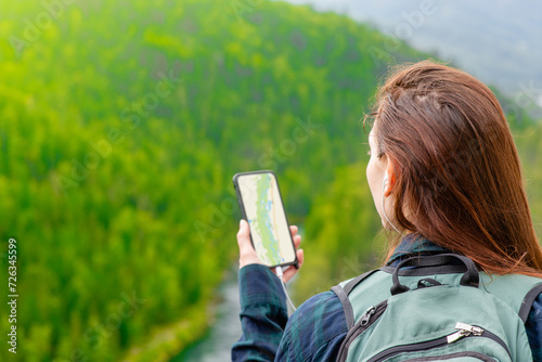 Young woman uses smartphone at sunny mountains and using travel app or map during her hike. Empty space for text