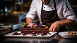 Close-up of a pastry chef decorating a chocolate dessert in a white plate before serving at the hotel restaurant. Cake, food, confectionery concepts.