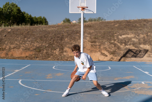 Young boy practicing dribbling while playing basketball on an outdoor court. Sports concept. © JoseIMartin
