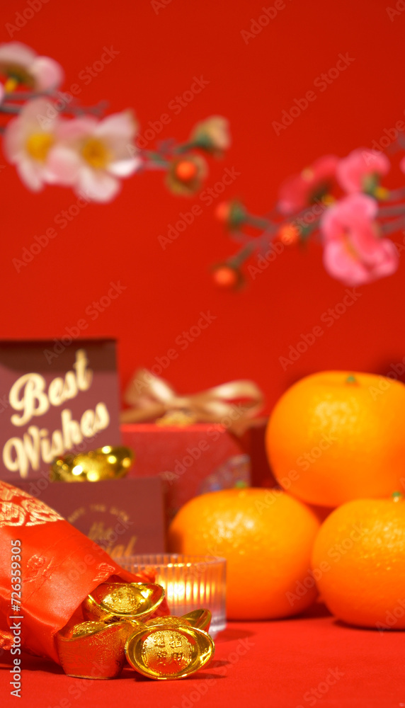 Chinese Lunar New Year red background. ancient Chinese ingot gold bar in silk bag, gift box with text best wishes, orange, paper fan, plum blossom, candle sway on Chinese new year celebrate