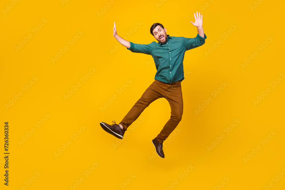 Full length photo of childish playful man dressed dotted shirt flying hands up fooling around isolated on vibrant yellow color background