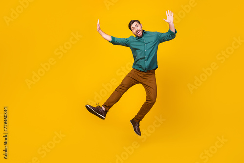 Full length photo of childish playful man dressed dotted shirt flying hands up fooling around isolated on vibrant yellow color background