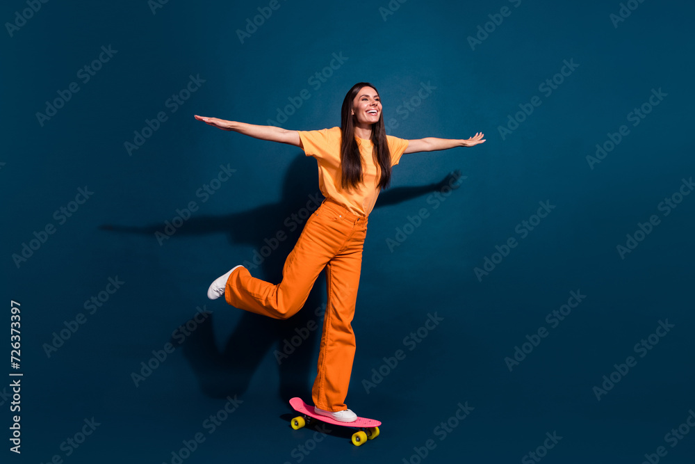 Full length photo of young brunette lady ride long board wings arms carefree chilling in skate park isolated on dark blue color background