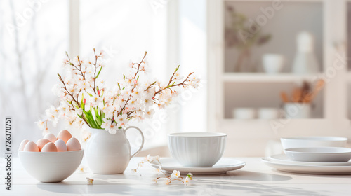 Photo of a light white kitchen, dishes with Easter eggs on the table, morning. Flowers in a vase, white dishes and fresh eggs, a healthy breakfast