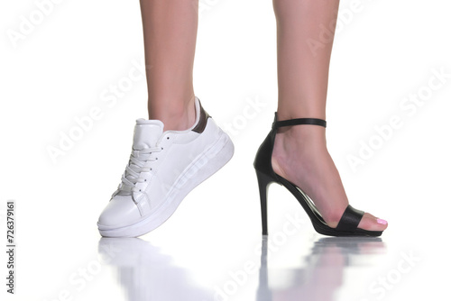 Closeup of female feet, one with sneakers, other in high heel shoe on white background
