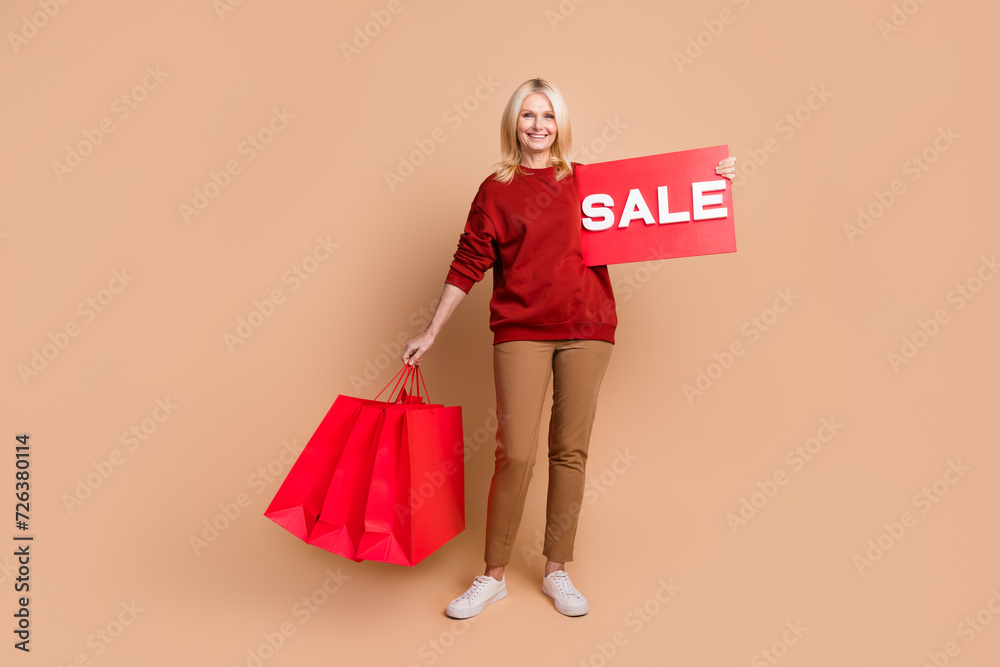 Full length photo of cheerful good mood woman wear red sweater holding sale billboard shoppers isolated beige color background Full length photo of cheerful good mood woman wear red sweater holding sale billboard shoppers isolated beige color background