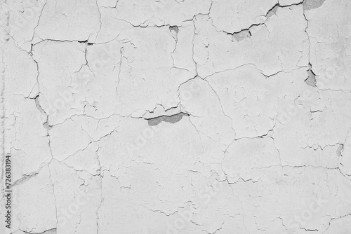 Peeling white paint on the concrete wall with old cracked flaking paint. Weathered rough painted surface with patterns of cracks and peeling. \ texture for background