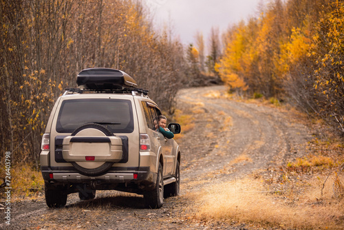 A woman sitinng in a SUV on а scenic autumn road in the forest and smiling