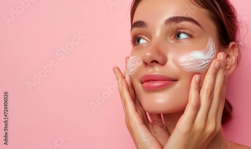 Young beautiful smiling woman takes care of her face skin. Woman puts cream on her face. Portrait of a woman on a pink background. Banner with space for text.