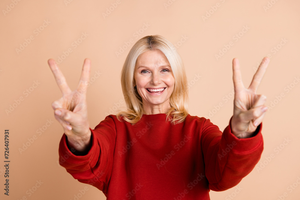 Photo of cheerful positive lady dressed red pullover showing you two v-signs isolated beige color background Photo of cheerful positive lady dressed red pullover showing you two v-signs isolated beige color background