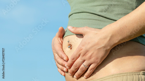 Pregnant woman park with navel piercing two months pregnant outdoors. Navel piercing on pregnant belly pointing with hands. Real image photo