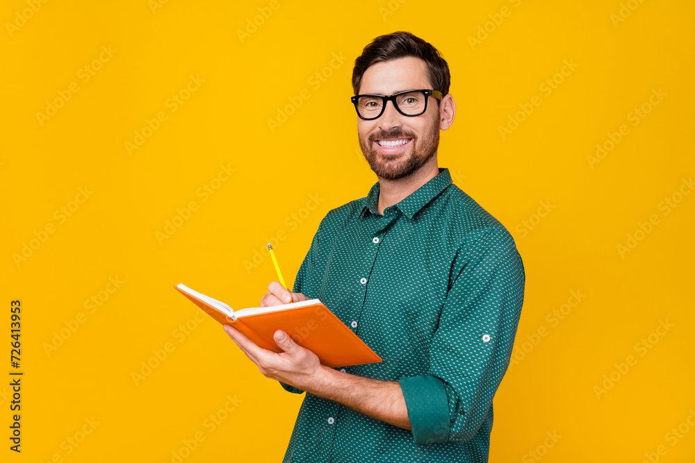 Photo of toothy beaming man with stylish haircut dressed dotted shirt in eyewear writing his own book isolated on yellow color background Photo of toothy beaming man with stylish haircut dressed dotted shirt in eyewear writing his own book isolated on yellow color background