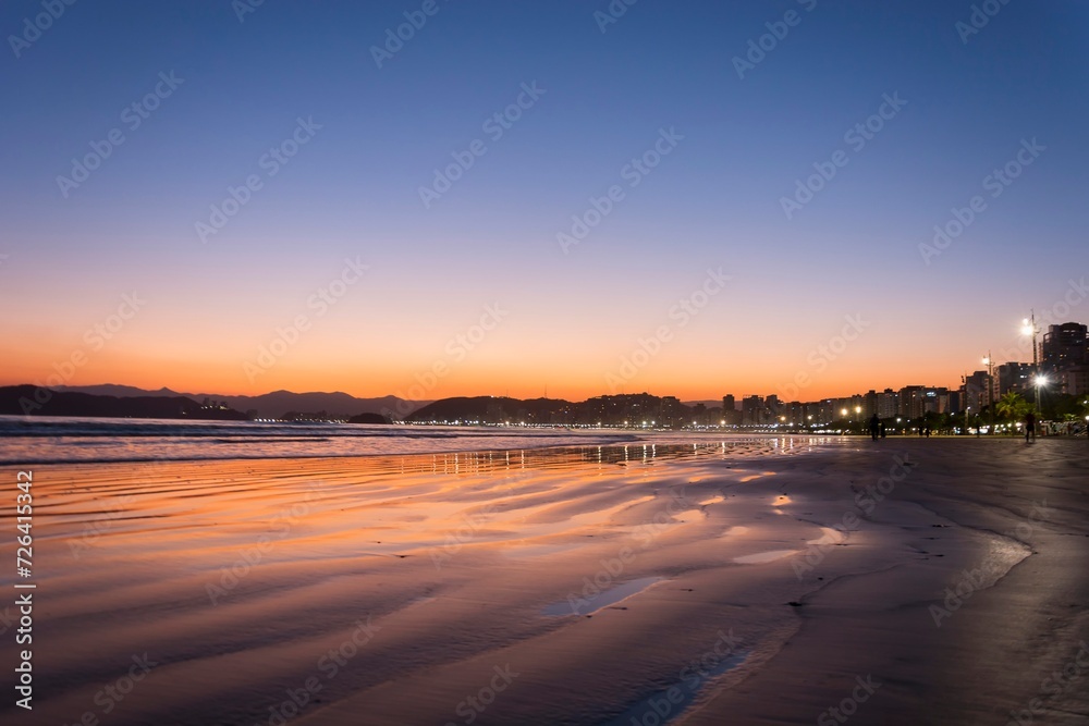 City of Santos, Brazil. Sunset at the beach. Reflection of the sky in the water mirror on the sand strip.