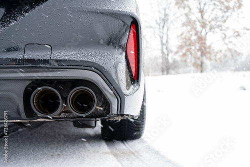 Double pipe exhaust system with carbon fairing on a black new sports car in winter while it is snowing photo