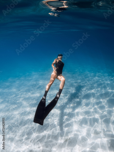 Freediver swimming underwater in sea over sandy bottom. Female swims with fins undersea