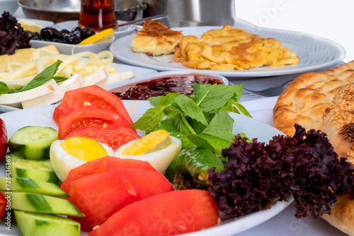 Close up of traditional turkish mixed breakfast table with various food such as boiled egg, tomato, cucumber, pepper, jams, cheese, cream, lettuce, pastry, fresh mint, olives, pita bread and tea.