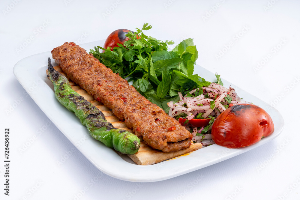 Top view of traditional grilled Adana kebab with cooked spicy shish kebab, pepper, tomato, and fresh greenery on a white plate isolated on white background. Top view of traditional grilled Adana kebab with cooked spicy shish kebab, pepper, tomato, and fresh greenery on a white plate isolated on white background.