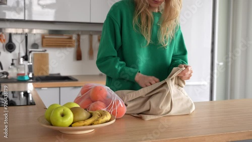 Woman using reusable bags for her shopping. Caucasian female takes out the fruits of the bag. Sustainable shopping concept.