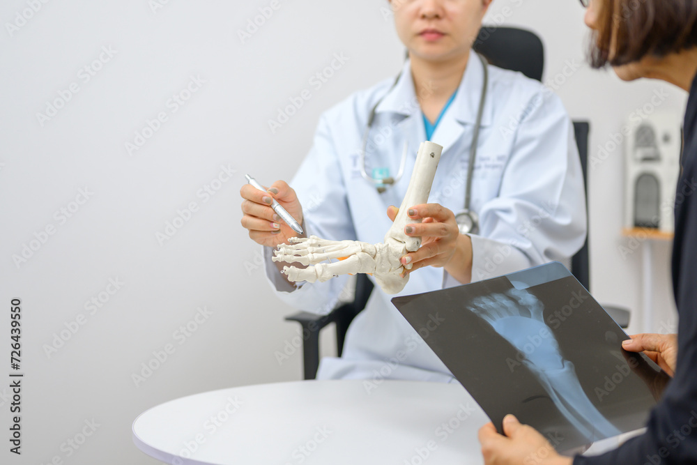 Asian female orthopedist Pointing to the ankle and foot bone model is explaining the patient's foot bone problems. Concept of health care for feet and foot bones Asian female orthopedist Pointing to the ankle and foot bone model is explaining the patient's foot bone problems. Concept of health care for feet and foot bones