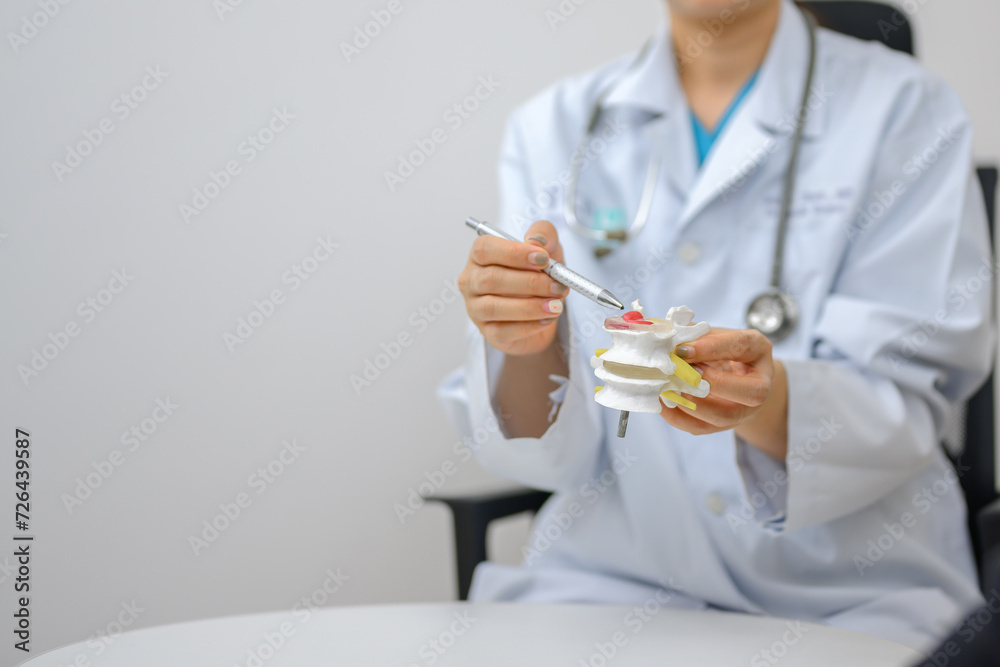 Picture of a close-up of an orthopedic doctor pointing at a spinal model and explaining to a patient her spinal problems. Health care and spine concept Picture of a close-up of an orthopedic doctor pointing at a spinal model and explaining to a patient her spinal problems. Health care and spine concept