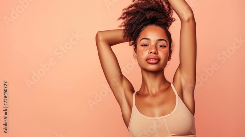 Young African American woman with freckles raising her arm, against a soft pink background