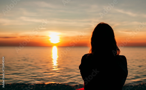 a woman sitting watching a sunset at the sea
