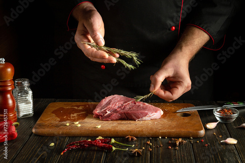 The cook is preparing a meat steak. Adding rosemary to lamb before grilling.