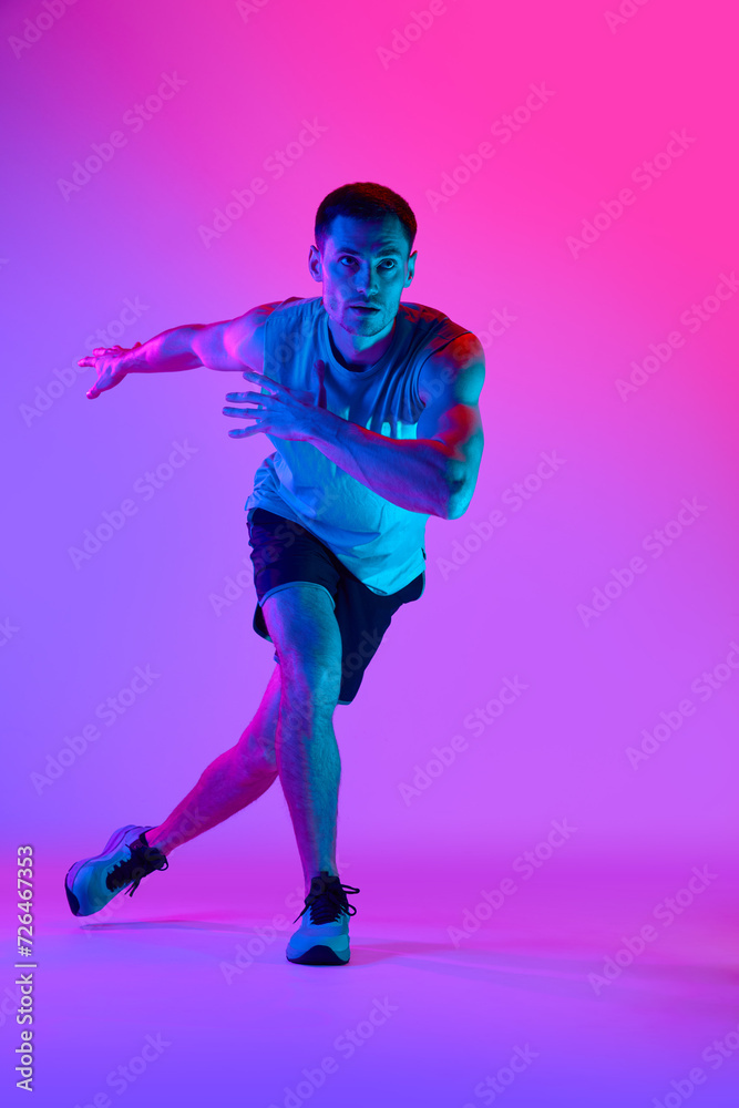 Athletic man in comfortable sportswear, with muscular body training against gradient pink background in neon light. Concept of active and healthy lifestyle, sport, fitness, endurance