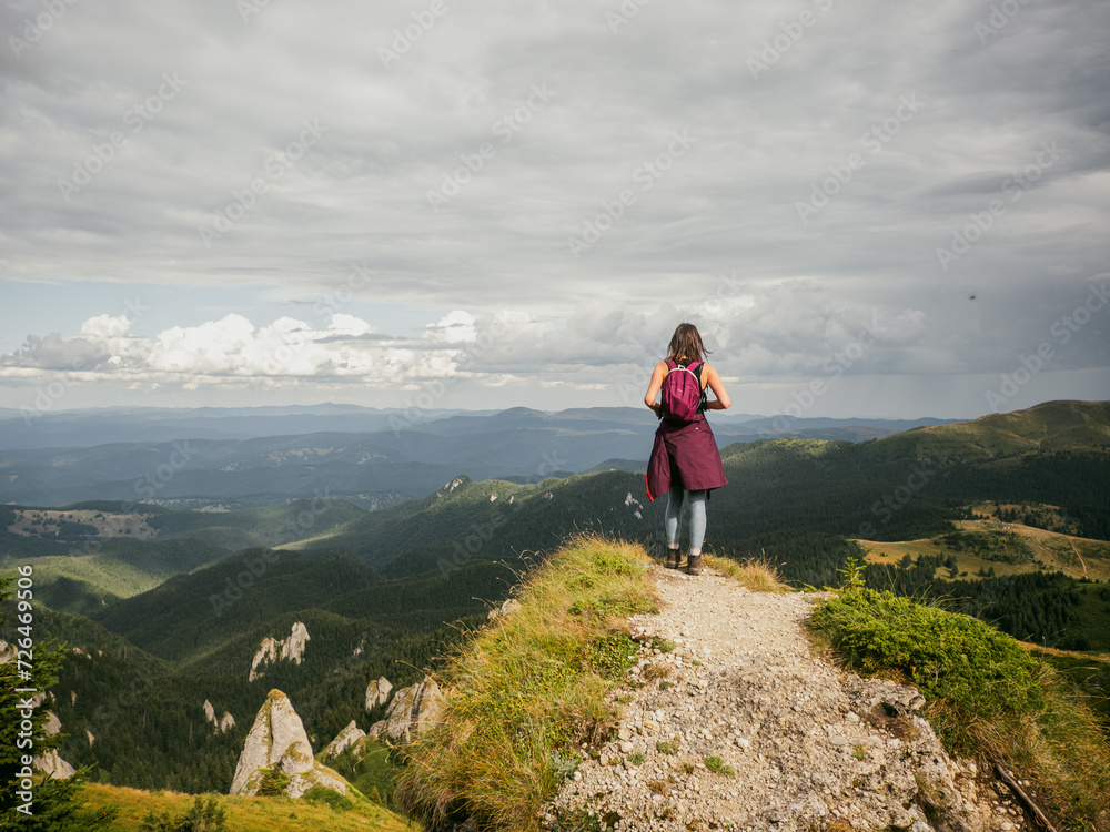 Girl standing on a cliff, admiring the alpine view of Carpathian mountains