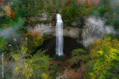 Falls Creek Falls is surrounded by vibrant fall colors and a misty morning haze. The waterfall cascades from a rocky cliff into a dark pool below. Photographed  at Falls Creek Falls State Park in TN