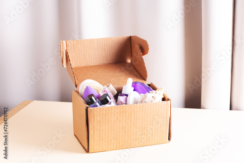 Open cardboard beauty box with various body care and skin care sample products in home interior.